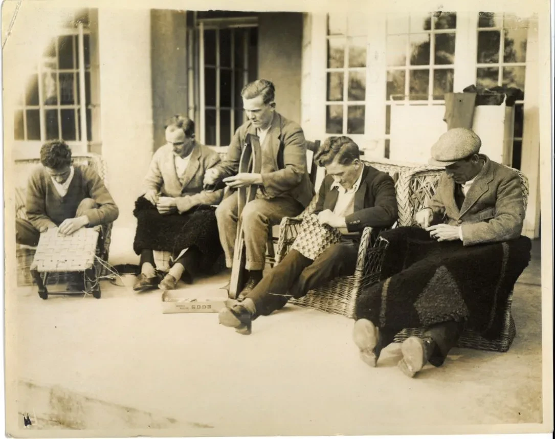 5 men seated making baskets